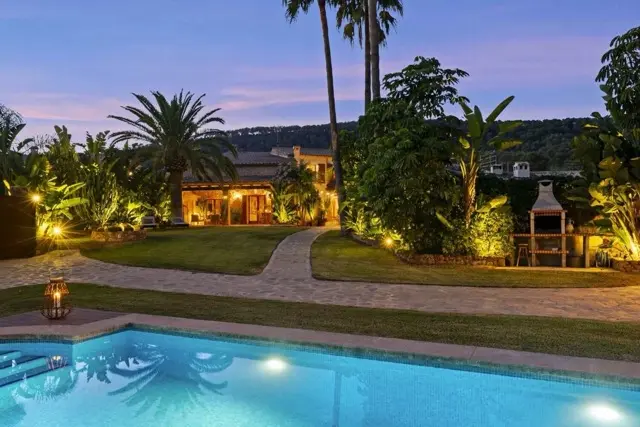 Mediterrane Finca auf Mallorca in der Dämmerung mit beleuchtetem Pool, Palmen und gepflegtem Garten