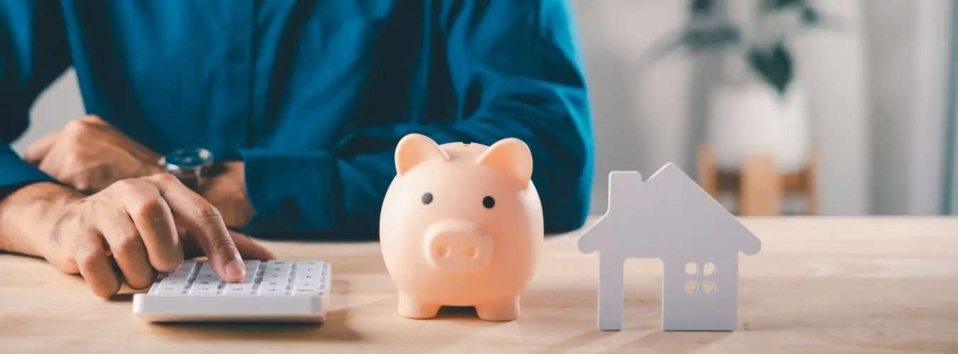 Mann nutzt Taschenrechner neben einem kleinen Hausmodell bei der Finanzplanung, Immobilienkauf über die Bank
