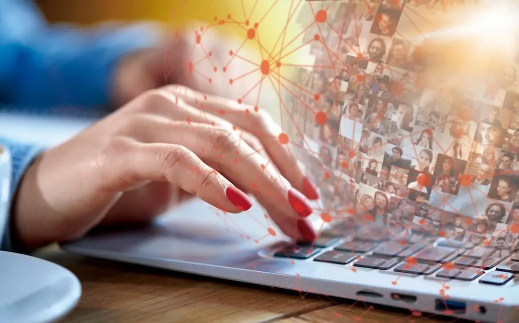 Hände mit roten Fingernägeln tippen auf Laptop-Tastatur, im Hintergrund ein digitales Netzwerk aus Profilfotos