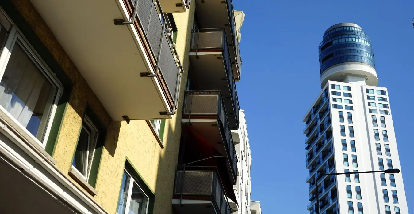 Gelbe Fassade eines Wohnhaus mit Balkons im Stil der Sechzigerjahre und moderne Architektur des neuen Henninger Turm vor blauem Himmel bei Sonnenschein am Hainer Weg in Frankfurt am Main Sachsenhausen