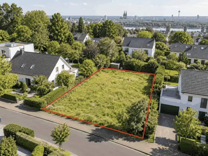 Unbebautes Baugrundstück in Köln, rot markiert zwischen Einfamilienhäusern, im Hintergrund die Skyline mit Kölner Dom
