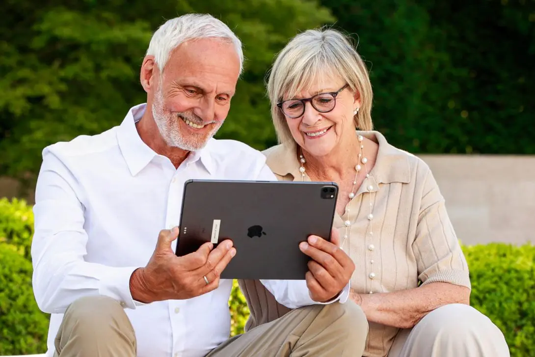 Älteres Ehepaar sitzt lächelnd im Garten und lässt online den Wert seiner Immobilie in Speyer auf einem Tablet einschätzen
