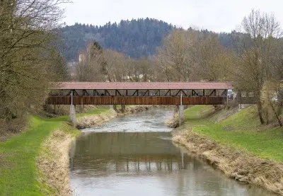 Historische überdachte Holzbrücke über einen Fluss im Hunsrück, umgeben von bewaldeten Hügeln