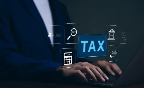 Businessman working on a laptop, surrounded by tax icons on a dark background.