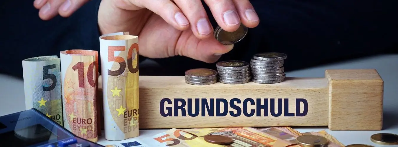 Grundschuld. Hand baut Geldstapel auf einem Baustein mit Text. Turm aus Euro Münzen. Taschenrechner daneben.