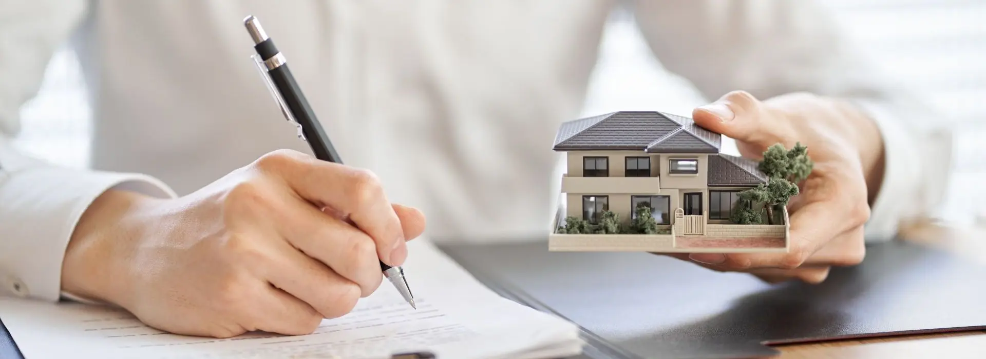 L'homme écrit quelque chose et tient dans l'autre main une petite maquette de maison.