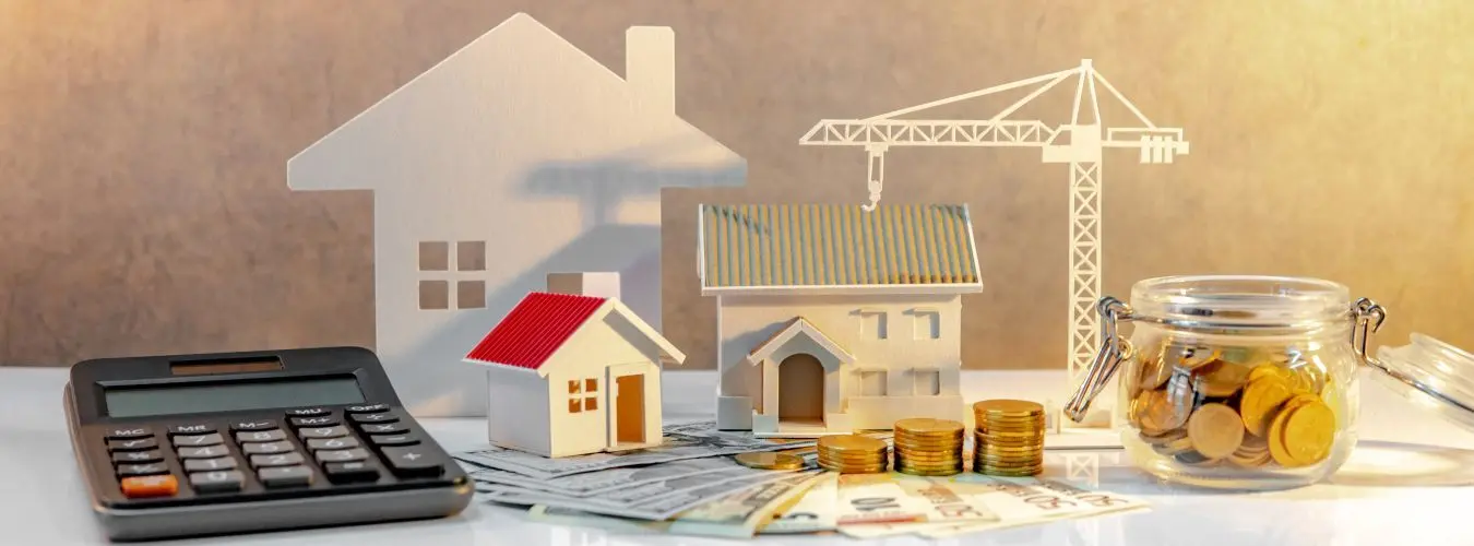 Développement immobilier. Pile de pièces sur des billets internationaux avec calculatrice, modèles de maisons et de grues