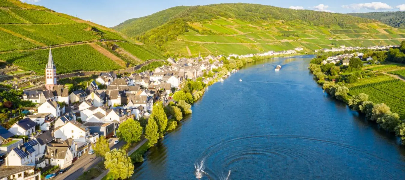 Heruntergeladen Hills with vineyards and church in Merl village of Zell (Mosel) town, Rhineland-Palatinate, Germany. Water skiing, barges, speedboats on the Moselle river